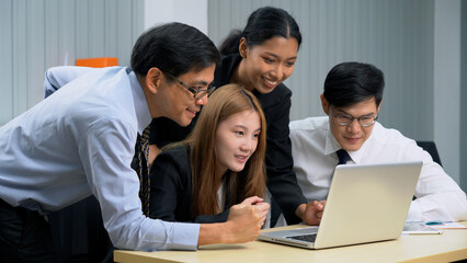 Group of happy asian business people sitting on a table raised fists cheering at laptop celebrating achievement goals to success in meeting at office