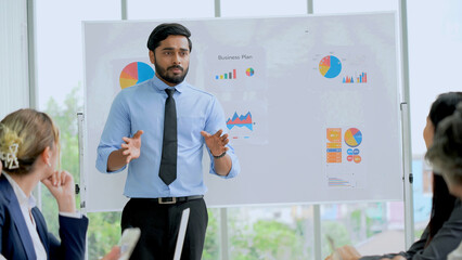Young indian business manager standing and presenting to multiracial group of diversity colleagues in front of white board in meeting at boardroom in office . leader