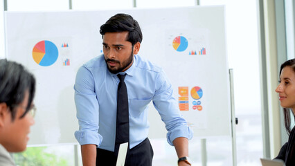 Young indian business manager standing and presenting to multiracial group of diversity colleagues in front of white board in meeting at boardroom in office . leader