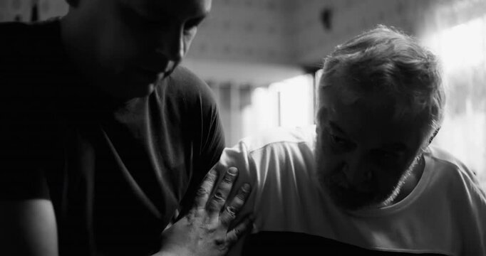 Man assisting an elderly man with dementia or age-related illness in a kitchen, gentle hand on shoulder, showing compassion and connection, black and white