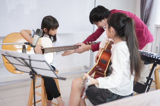 teen asian girls take guitar lesson in a music tutoring,elementary age students learning a new skill music during school break