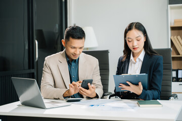 Fototapeta premium Two business workers talking on the smartphone and using laptop at the office..