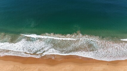 Drone shot aerial view at a beach of waves crashing onto the shore in Australia 
