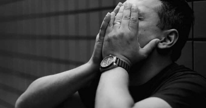 Close-up of man in emotional crisis, leaning against wall with clasped hands, intense mental struggle, depression, inner turmoil, profound despair and pain, black adn white