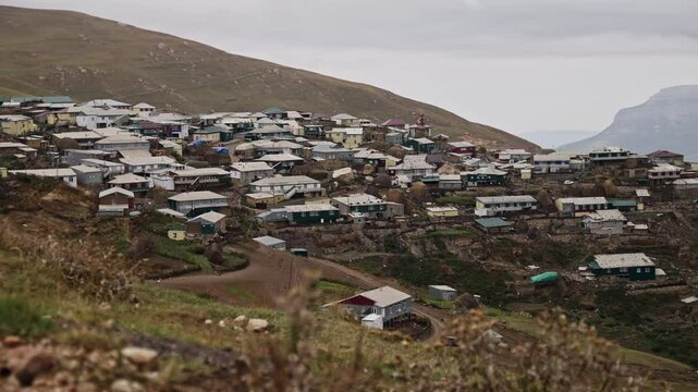 Xinaliq mountain village nestled on rocky hillside, revealing weathered stone dwellings against cloudy caucasus landscape, representing azerbaijani highland cultural heritage