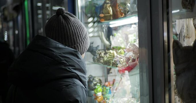 Retail, night city. A young woman in winter clothes smiles looking at the illuminated souvenir window of a small shop. Hand held. Siberia.