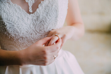 A woman is wearing a white wedding dress and holding a ring in her hand. The dress is adorned with lace and the ring is a gold band. Concept of elegance and celebration
