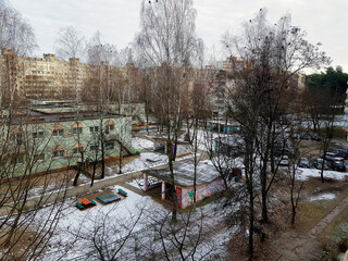 Winter landscape reveals a quiet urban space with bare trees and remnants of snow in the background