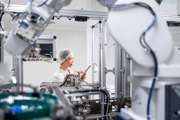 Japanese engineer working in automated robotic production line and controlling and monitoring production process of modern industrial machine. Robotic arm manufacturing electronics equipment.