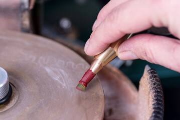 Close-up view of the craftsman faceting a round peridot stone attached on a metal dop