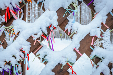 A close-up of a wooden lattice adorned with vibrant ribbons in various colors, partially covered by...