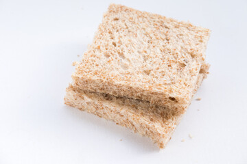 Two slices of whole wheat bread on a white background. The bread has a light brown color and visible texture with small air pockets and bran flecks.