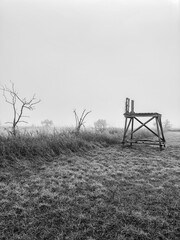 Naklejka premium Black and white photo of a high seat on a foggy field covered with hoarfrost in winter.