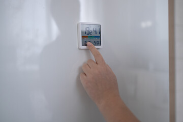 Woman hand lowering the temperature for energy saving. Woman adjusting digital central heating thermostat at home.