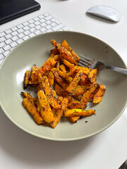 Plate of perfectly roasted vegetables seasoned with herbs, placed on a desk with a keyboard nearby. Concept of healthy eating during work breaks, blending productivity with mindful nutrition