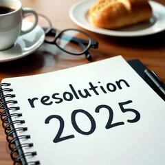2025 resolution notebook, with pen, glasses, bread and a cup of coffee