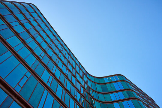 Low angle view of modern curved high rise building. Glass facade of skyscraper. Office building against blue sky. Contemporary architectural design