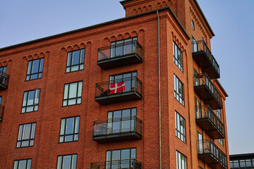 Red brick apartment building with balconies and Danish flag hanging from one of balcony in Copenhagen, Denmark