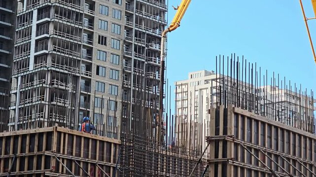 Construction workers and concrete pump at high rise building construction site. Reinforcement steel bars, formwork and residential development project with modern apartment towers in background. Mediu