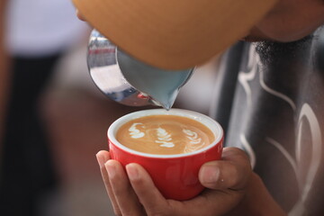 Milk pours into cup creating coffee art by barista.