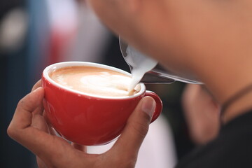 Milk pours into cup creating coffee art by barista.