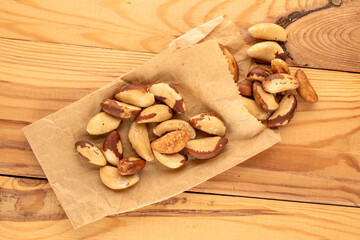 Brazil nuts without shells with  paper bag on wooden table, close-up, top view.
