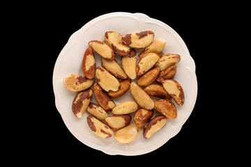 Brazil nuts without shells on a white ceramic plate on a black background, close-up, top view.