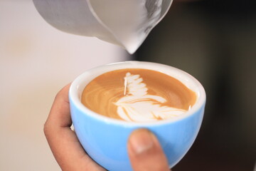 Milk pours into cup creating coffee art by barista.
