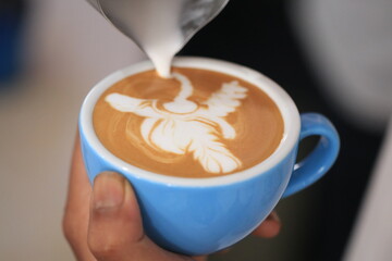 Milk pours into cup creating coffee art by barista.
