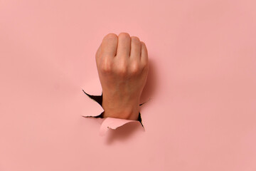 Hand breaking through pink paper wall with clenched fist. Conceptual studio shot for creative...