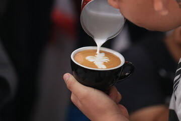 Milk pours into cup creating coffee art by barista.