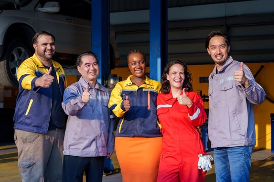 Group of diverse mechanics smiling and posing in an auto repair shop. Unity and collaboration symbolized through bright uniforms, teamwork, and friendly professionalism in an industrial setting.