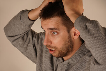 Fototapeta premium His face reflects a moment of suffering. The pose creates an irresistible feeling of mental tension. Holding his hair in his fist, the man shows clear signs of tension or stress.