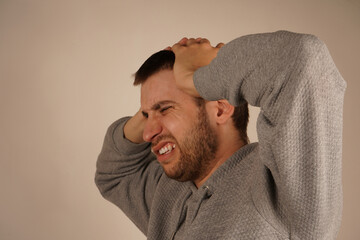 A man holds both hands on his head, a gesture that indicates stress or mental tension. His facial...