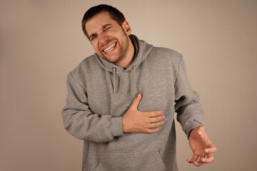 The expression suggests a burning sensation or severe discomfort. It could indicate heart failure symptoms. A man in a gray hoodie holds his chest near the ribs with one hand, his face showing pain.