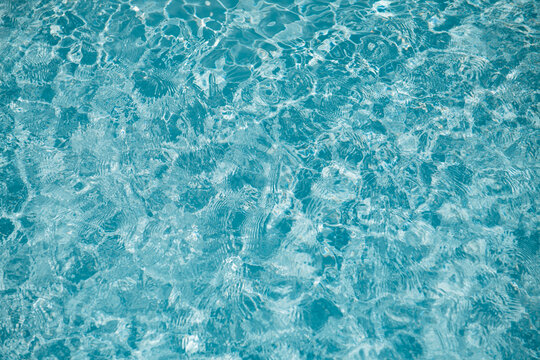 crystal clear blue water surface in swimming pool or ocean with ripples and sunlight reflection background