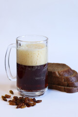 Mug of tasty kvass, bread and raisins on light background. Glass mug of kvass with foam, close-up. Kvass with ingredients on white background. Refreshing drink with slices of bread, selective focus