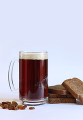 Mug of tasty kvass, bread and raisins on light background. Glass mug of kvass with foam, close-up. Kvass with ingredients on white background. Refreshing drink with slices of bread, selective focus