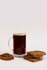 Mug of tasty kvass, bread and raisins on light background. Glass mug of kvass with foam, close-up. Kvass with ingredients on white background. Refreshing drink with slices of bread, selective focus