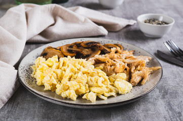 Scrambled eggs, fried chicken and champignons on a plate on the table
