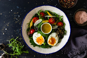 Fresh green salad with vegetables, boiled eggs and vinaigrette sauce on black table