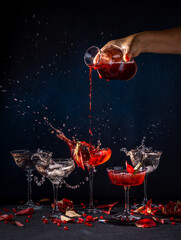 Bartender pouring red drink into cocktail glass, creating splash with pomegranate seeds