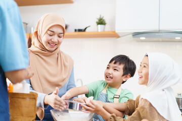 Fototapeta premium Happy Asian muslim family consisting father, mother, son, and daughter are cooking together in the kitchen.