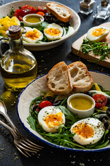 Fresh green salad with vegetables, boiled eggs and vinaigrette sauce on black table