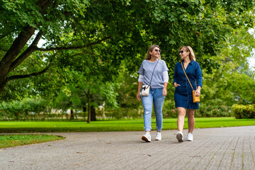 Two smiling mature women walking in city park. Meeting of friends. Walk in park	