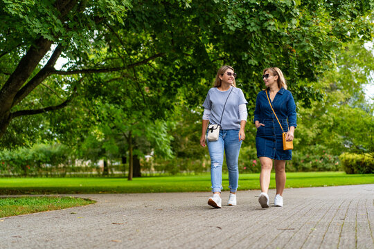 Two smiling mature women walking in city park. Meeting of friends. Walk in park	