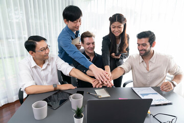 Group of diverse office worker join hand together in office room symbolize business synergy and strong productive teamwork in workplace. Cooperation and unity between business employee. Prudent