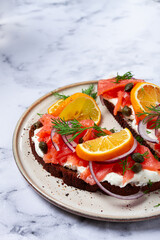 sandwich with freshly smoked salmon, on black bread, with cottage cheese, with herbs and red onions, capers and pieces of citrus fruits, on a marble countertop, breakfast, no people,
