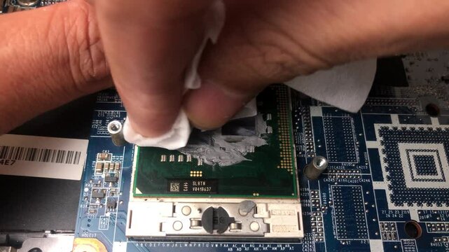 A computer technician hand carefully cleans the remaining thermal paste on a laptop processor using a tissue
