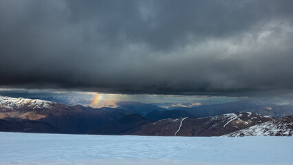 Arc en ciel en montagne entre nuages menaçants et neige